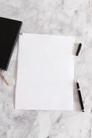 a4 vitt blankt papper på marmorbakgrund med en penna och anteckningsbok, mockup foto