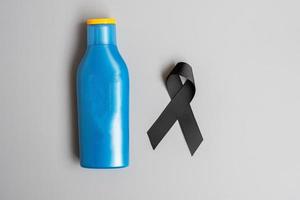 månad för medvetenhet om melanom och hudcancer. svart band och kropp solskyddsmedel flaska på grå bakgrund. världen cancer dag koncept foto