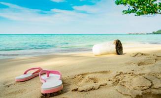 rosa och vita sandaler på sandstranden. casual stil flip-flop togs bort vid havet. sommarsemester på den tropiska stranden. rolig semesterresa på sandstranden. sommartid. sommarvibbar. avslappnings tid. foto