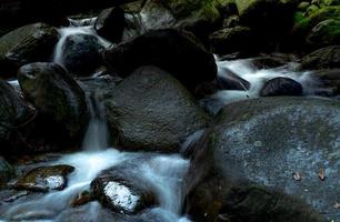 svart sten vid vattenfallet med grön mossa och solsken på sten. vattenfallet rinner i djungeln. vattenfall i tropisk skog. natur bakgrund. grön säsong resor. ekoturism. vattenfall i det vilda. foto