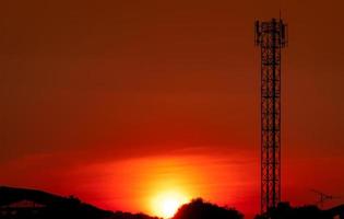 vacker röd och orange solnedgångshimmel. siluett telekommunikation torn och träd på kvällen med vacker röd solnedgång himmel och moln. natur bakgrund. foto