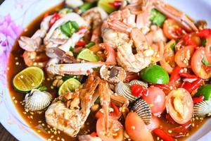kryddig sallad skaldjur på bricka, sallad thailändsk mat kryddig läcker skaldjur med krabba räkor hjärtmussla bläckfisk och kryddor ingrediens citron lime tomat färsk chili kryddig mat foto