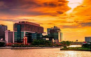 stadsbild av modern byggnad nära floden på morgonen vid soluppgången. modern arkitektur kontorsbyggnad i thailand. riverfront byggnad och stad med orange himmel och moln foto