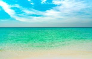 gyllene sandstrand vid havet med smaragdgrönt havsvatten och blå himmel och vita moln. sommarsemester på tropiskt paradisstrand koncept. krusning av vatten stänk på sandstrand. sommarvibbar. foto
