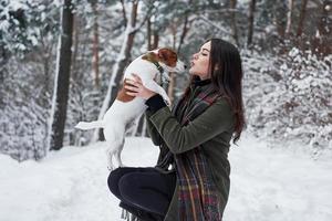 sidovy. leende brunett ha kul när hon går med sin hund i vinterparken foto