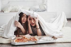 thriller på skärmen. varm filt. systrar äter pizza när de tittar på tv medan de ligger på golvet i det vackra sovrummet på dagtid foto