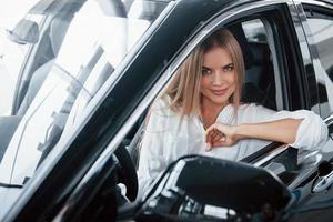 genom fönstret. vacker blond tjej sitter i den nya bilen med modern svart interiör foto