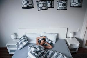 helgerna har kommit. kvinna med ögonbindel mask för en sömn ligger på sängen på morgonen foto