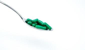 gröna antibiotika kapsel piller i rostfri sked isolerad på vit bakgrund med kopia utrymme för text och urklippsbana. aknebehandling, hälsopolicy och sjukförsäkringskoncept. foto
