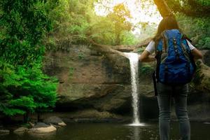 bakifrån av asiatisk kvinna med ryggsäck tittar på litet vattenfall i djungeln. aktiv kvinna med äventyrsresor i grön skog. vandring eller vandring tjej. utomhusaktivitet. vattenfall vid berget. foto