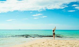 glad ung kvinna i vita skjortor och shorts som går på sandstranden. koppla av och njuta av semestern på den tropiska paradisstranden med blå himmel och moln. flicka i sommarlovet. sommarvibbar. glad dag. foto