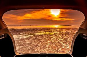 vacker havsutsikt inifrån bilens bagageutrymme. havsutsikt med orange himmel och moln i solnedgångstid på stranden. frihet sommar resor med road trip på semester koncept. romantisk utsikt på kvällen. foto