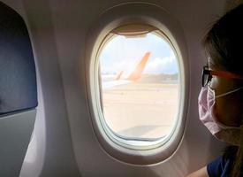sjuk kvinna bär ansiktsmask sitta på passagerarsäte nära kabinfönstret i flygplan. passagerare i avgångsflygplan på flygplatsen. ny coronavirus covid-19 infektion eller wuhan coronavirus foto