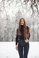 ung modell. söt flicka med långt hår och i svart blus är i vinterskogen foto