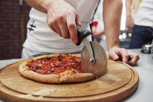 med hjälp av speciell anordning för skärning. bild av förberedd läcker pizza med korvringar och oliver foto