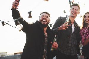 trevligt skratt. grupp av unga glada vänner har roligt medan de tar selfie på taket med dekorera glödlampor foto