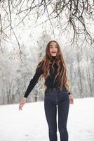 smal kroppstyp. söt flicka med långt hår och i svart blus som dansar i vinterskogen foto