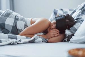 äntligen helg. kvinna med ögonbindel mask för en sömn ligger på sängen på morgonen foto