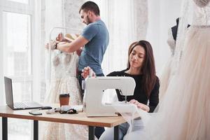 anställd bakom. kvinnlig modedesigner jobbar på de nya kläderna i verkstaden med mannen bakom foto