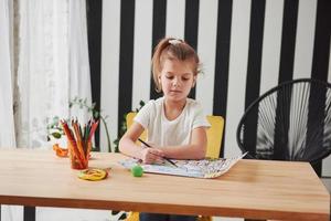 seriös blick. söt liten flicka i konstskola ritar sina första målningar med pennor och markörer foto