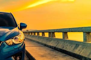 lyxig blå suv-bil med sport och modern design parkerad på betongväg vid havet i solnedgången. hybridbil och bilkoncept. roadtrip och bilkörning för resor. elbil teknik koncept foto
