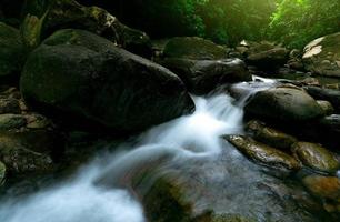 vackert vattenfall i djungeln. vattenfall i tropisk skog med grönt träd och solljus. vattenfallet rinner i djungeln. natur bakgrund. sten eller sten vid vattenfallet. grön säsong resor i thailand foto