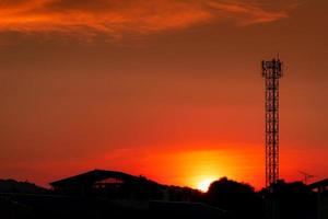 vacker röd och orange solnedgångshimmel. siluett telekommunikation torn och träd på kvällen med vacker röd solnedgång himmel och moln. natur bakgrund. foto