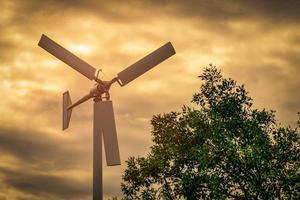 horisontell axel vindturbin med blå himmel och vita moln nära grönt träd. vindenergi i eko vindkraftspark. grön energi koncept. förnyelseenergi. alternativ elkälla. hållbara resurser. foto