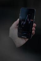 manlig hand som håller smartphone med finansiellt valutadiagram på skärmen foto