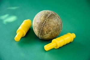 närbild gammal cricket sport utrustning på grönt golv, gammal läder boll och gula plast wickets, mjukt och selektivt fokus, traditionell cricket sport älskare runt om i världen koncept. foto