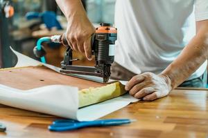 snickare med spikpistol eller häftpistol efter att ha bytt ut ett vinyl- eller klädseltyg till sätet för barstolar, möbelrestaurering träbearbetningskoncept. selektiv fokusering foto