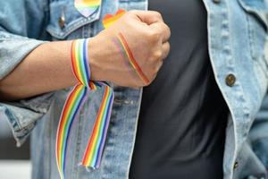 asiatisk dam som bär regnbågsflaggarmband, symbol för HBT stolthet månad firar årliga i juni sociala av homosexuella, lesbiska, bisexuella, transpersoner, mänskliga rättigheter. foto