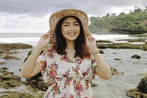 en ung asiatisk tjej som bär strandhatt kopplar av på stranden med blå himmel i gunungkidul, Indonesien foto