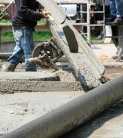 arbetare man håller mixer cement lastbil häll vätska betongrör till golvet hus. grupp av arbetare arbetsmaterial på plats. foto
