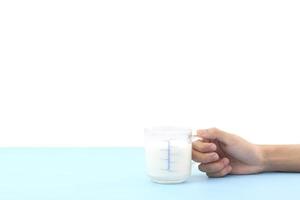världens mjölkdag koncept - handhåll glas färsk kall rustik komjölk - högt protein och kalcium på blått bord mot vit bakgrund till frukost på morgonen. foto