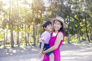 asiatisk pojke och mamma kvinna kopplar av på tropisk strand, de är njoy frihet och frisk luft, bär snygg hatt och kläder. glad leende turist i tropikerna i resesemester foto