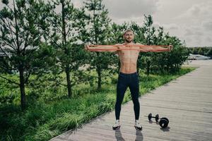 träning, hälsosam livsstil och bodybuilding koncept. stark muskulös europeisk man sträcker ut motståndsbandet, bär sneakers, står utomhus, tycker om att träna utomhus, har atletisk kropp. foto