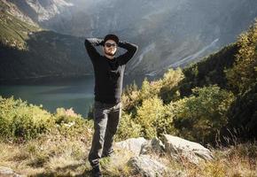 ung turist man i en mössa med händerna upp på toppen av bergen foto