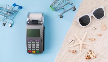 ovanifrån av kreditkort och kortläsare maskin med faktura räkning och sjöstjärna, solglasögon på sand. foto