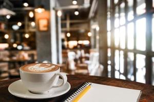 kaffearom i kopp frukost morgondrink på träbord i cafébutik med anteckningsblock och tidningsrestaurang foto