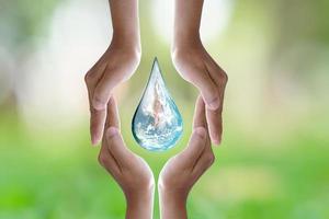 världsmiljö day.human hand skyddar vattendroppe med solljus på grön natur bakgrund. foto