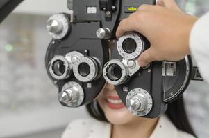 ung kvinnlig kund undersöks visuellt test med hjälp av bifokal optometri synmätningsanordning av ögonläkare i optiskt centrum, ögonvårdskoncept. foto