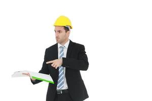 stilig och smart ingenjör i svart kostym bär en gul säkerhetsteknisk hatt med hand som håller konstruktionsritningspapper och seriös i arbete isolerad på gul bakgrund. foto