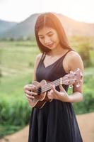 vacker kvinna som håller en gitarr på axeln, naturpark sommar utanför. foto