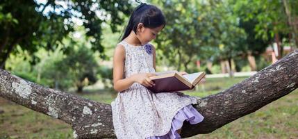 liten söt asiatisk flicka som läser bok i naturen. foto