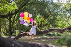 ung tonåring flicka sitter på träd och håller ballonger i handen foto
