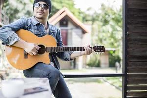 ung hipster man spelar gitarr för att koppla av på sin semester, njuta med naturlig och frisk luft. foto