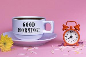 god morgon text på vit kaffekopp med väckarklockan inställd på klockan 8. foto