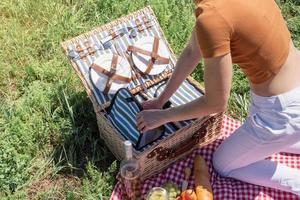 ung kaukasisk kvinna förbereder picknickkorg utomhus, redo att ha en picknick foto