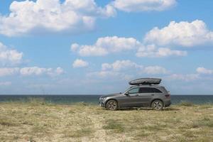 crimea, Ukraina, 22 juli 2021 - Mercedes Benz suv med takräcke, mot bakgrund av den vilda Svarta havets kust och molnen. foto